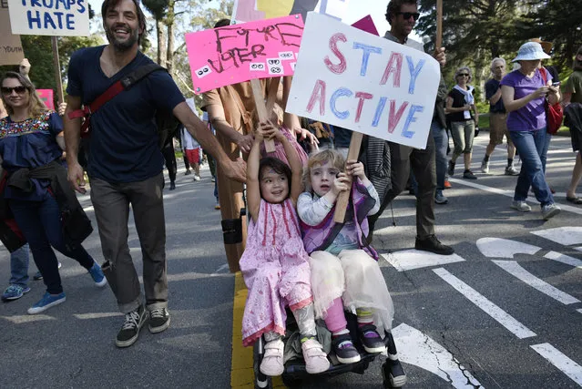 Veda Bartels, 3, left, and Edie Marshall, 4, hold up signs while riding in a stroller during an anti-Trump march through Golden Gate Park in San Francisco on Sunday, November 13, 2016. Hundreds of people, including many families with children, marched from Golden Gate Park to Ocean Beach chanting “Love trumps hate!” (Photo by Michael Short/San Francisco Chronicle via AP Photo)