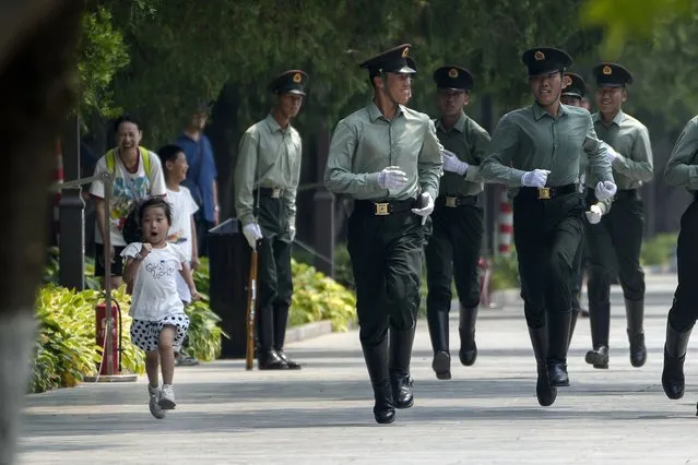 A girl runs along with members of an honor guard as they practice a march near the Forbidden City on the hot day in Beijing, Sunday, June 25, 2023. (Photo by Andy Wong/AP Photo)