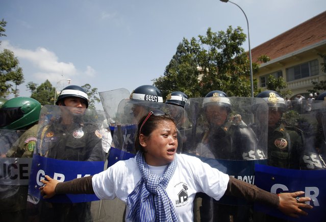 A woman reacts as police officers block the march along a street on the occasion of World Habitat Day in central Phnom Penh October 10, 2013. Residents of Boeung Kak lake, Borei Keila and other communities gathered on Thursday as they called on the Cambodian government to stop evicting them from their homes. World Habitat Day took place on October 7. (Photo by Samrang Pring/Reuters)