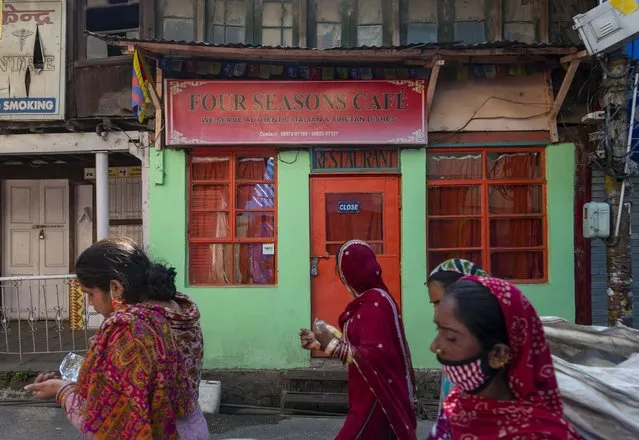 Sanitary workers, some wearing face masks as a precaution against the coronavirus, walk past a closed restaurant during lockdown imposed to curb the spread of the coronavirus in Dharmsala, India, Saturday, May 22, 2021. (Photo by Ashwini Bhatia/AP Photo)