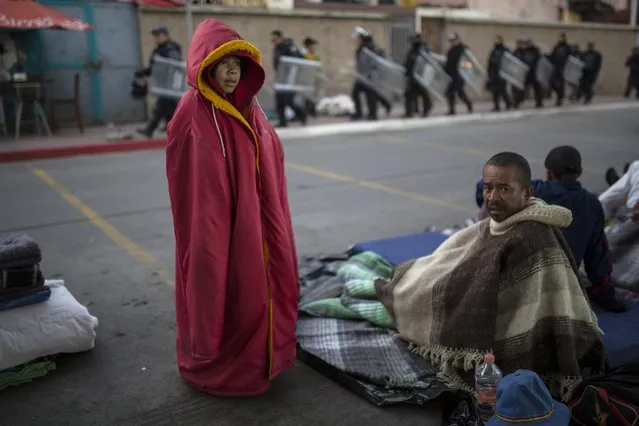 Jonathan Torres, 11, stands next to his father after waking up early in the morning as Mexican riot police make their way to the Chaparral border crossing, in Tijuana, Mexico, Friday, November 23, 2018. The mayor of Tijuana has declared a humanitarian crisis in his border city and says that he has asked the United Nations for aid to deal with the approximately 5,000 Central American migrants who have arrived in the city.(Photo by Rodrigo Abd/AP Photo)