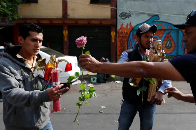 A follower gives a rose to another follower as a symbol of offering to the Santa Muerte or The Saint of Death during the first prayer of the New Year in Mexico City, Mexico January 1, 2017. (Photo by Carlos Jasso/Reuters)