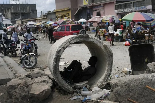 A man uses his cellphone inside a concrete pipe at a market in Cap-Haitien, Haiti, Thursday, July 22, 2021. (Photo by Matias Delacroix/AP Photo)