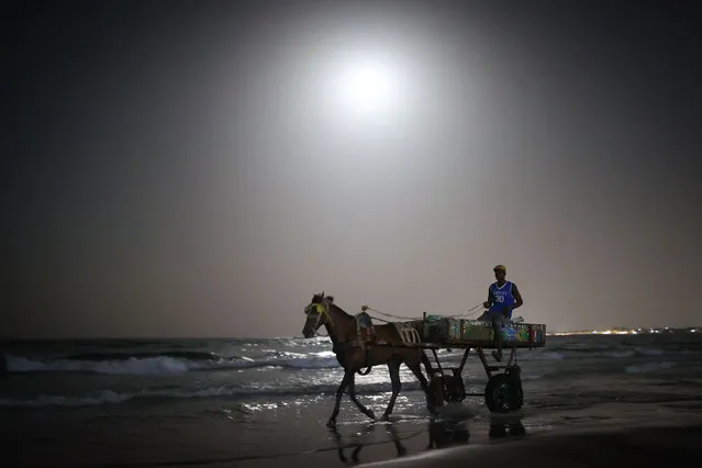 Workers carrying loads with horse carts on the ocean shore are seen in the light of the full moon appearing in the Yoff region, Dakar, Senegal on November 26, 2023. (Photo by Cem Ozdel/Anadolu via Getty Images)