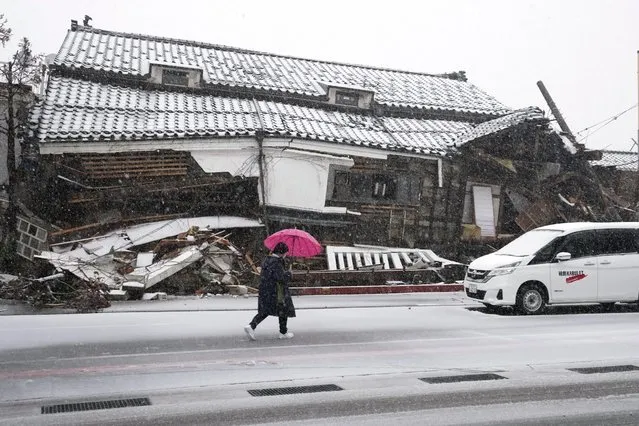 A person walks in the snow through a street near a damaged house in Wajima in the Noto peninsula facing the Sea of Japan, northwest of Tokyo, Sunday, January 7, 2024. (Photo by Hiro Komae/AP Photo)