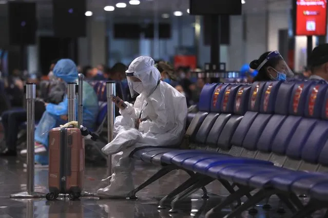 A passenger in full protective suit uses a phone while waiting to board a flight at Tan Son Nhat airport in Ho Chi Minh city, Vietnam Friday, October 15, 2021. Vietnam has resumed air travel after several months of suspension due to COVID-19 outbreak. (Photo by Hau Dinh/AP Photo)
