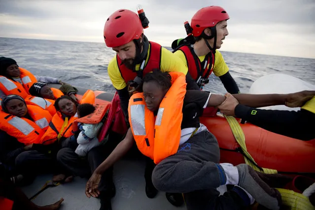 A woman is assisted by members of the Spanish NGO Proactiva Open Arms, as they crowd on board of a rubber boat sailing out of control in the Mediterranean some miles north of Sabratha, Libya, on Friday, February 3, 2017. European Union leaders are poised to take a big step on Friday in closing off the illegal migration routes from Libya across the central Mediterranean, where thousands have died trying to reach the EU, the EU foreign affairs chief Federica Mogherini said. (Photo by Emilio Morenatti/AP Photo)