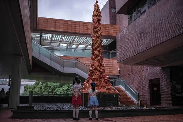 Two children look at the “Pillar of Shame” statue at the Hong Kong University campus on October 15, 2021 in Hong Kong, China. Hong Kong University demanded that a now-disbanded pro-democracy alliance remove the artwork, an eight-metre tall monument to the Tiananmen Square Massacre by Danish artist Jens Glaschiot, after it has stood on the grounds of the campus for 24 years, local news sources reported. The statue is an iconic art piece, one of several by the artist placed around the world commemorating similar events. (Photo by Louise Delmotte/Getty Images)