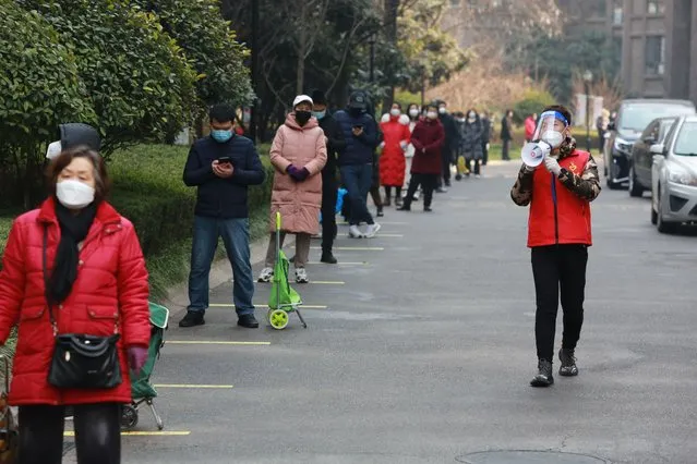 A community volunteer uses a megaphone to remind residents to keep their social distance as they line up to collect their daily necessities outside a residential block in Xi'an city in northwest China's Shaanxi province Monday, January 3, 2022. (Photo by Chinatopix via AP Photo)