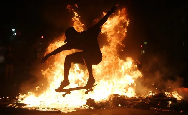 A young man practices a skateboarding move in front of a fire set by protestors following a demonstration against proposed federal government reforms on March 15, 2017 in Rio de Janeiro, Brazil. Protestors rallied nationwide, mostly peacefully, against proposed rules tightening pensions as the country continues to suffer through a financial and political crisis. (Photo by Mario Tama/Getty Images)