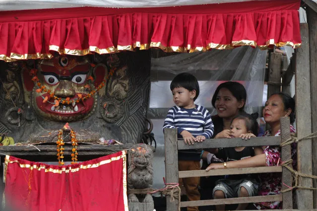 Devotees sit next to a statue of god Bhairabh during Indra Jatra festival, an eight-day festival that honors Indra, the Hindu god of rain, in Kathmandu, Nepal, Friday, September 13, 2019. The girl child revered as the Living Goddess Kumari is pulled around Kathmandu in a wooden chariot, families gather for feasts and at shrines to light incense for the dead, and men and boys in colorful masks and gowns representing Hindu deities dance to the beat of traditional music and devotees' drums, drawing tens of thousands of spectators to the city's old streets. (Photo by Niranjan Shrestha/AP Photo)
