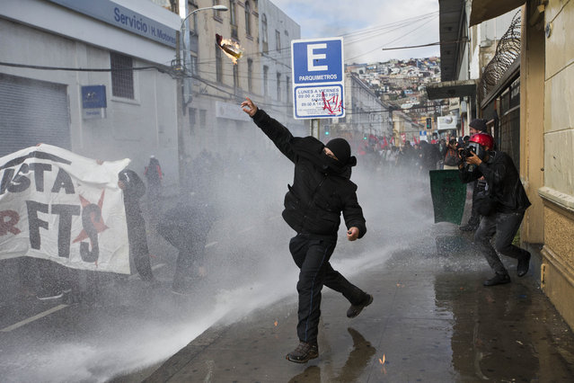 A masked protester launches a Molotov cocktail towards police, near Congress where President Michelle Bachelet was presenting the state-of-the-nation report, in Valparaiso, Chile, Saturday, May 21, 2016. (Photo by Esteban Felix/AP Photo)