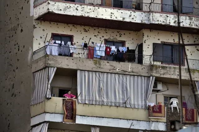 A woman hangs a rug on her balcony riddled by bullets from clashes between pro and anti-Syrian government groups, in Tripoli, Lebanon, February 16, 2022. Often known in recent years for sectarian and other violence, Tripoli seems an unlikely place for a cultural revival, but it has a long cinematic tradition, once boasting 35 movie houses and Lebanon's first cinema. Kassem Istanbouli, a 35-year-old actor and director is now seeking to restore some of that past glory by turning the city’s long abandoned Empire Cinema into a national theater. (Photo by Bilal Hussein/AP Photo)