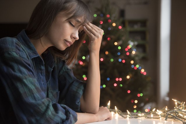 Mixed Race woman with headache near Christmas tree. (Photo by JGI/Jamie Grill/Getty Images)