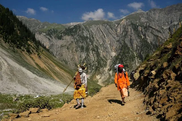 A Sadhu, or Hindu holy man, walks along a path next to another pilgrim during the pilgrimage to the cave shrine of Amarnath, near Baltal on June 30, 2022. (Photo by Tauseef Mustafa/AFP Photo)