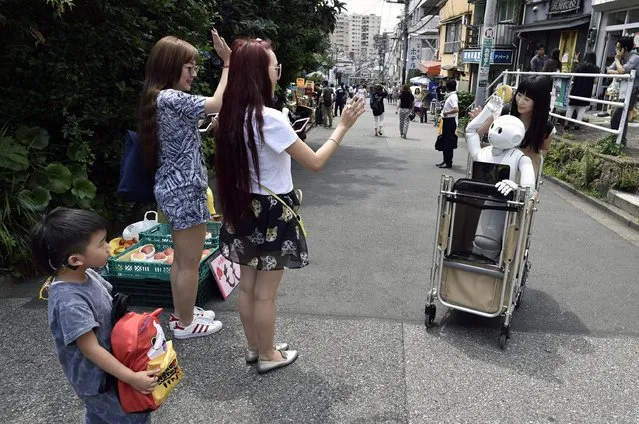 Tourists react as they see Tomomi Ota (R) pushing a cart loaded with her humanoid robot Pepper in Tokyo, Japan, 26 June 2016. (Photo by Franck Robichon/EPA)