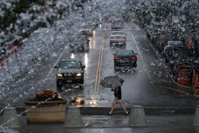 A water feature at Georgetown Waterfront Park appears to add to the already heavy rain as an umbrella clad pedestrian is framed by Wisconsin Ave. NW on Tuesday July 05, 2022 in Washington, DC. (Photo by Matt McClain/The Washington Post)