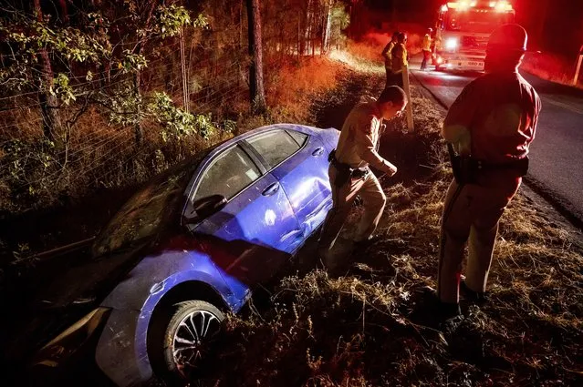 California Highway Patrol Officer Matthew Chance walks away from a car that crashed into a ditch while driving away from the Oak Fire in Mariposa County, Calif., on Friday, July 22, 2022. Chance gave the elderly driver a ride out of the fire evacuation zone. (Photo by Noah Berger/AP Photo)