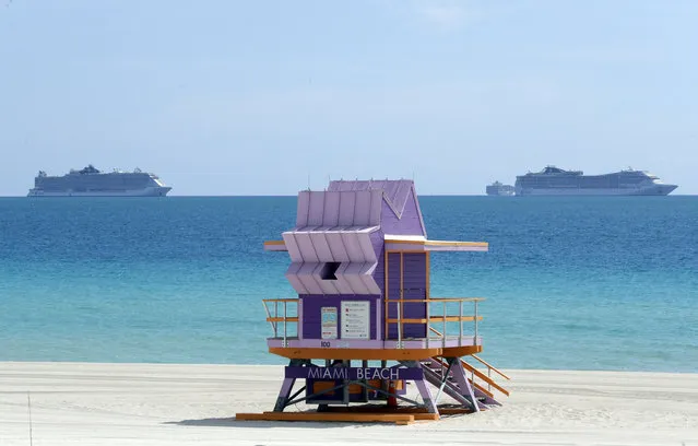 Two cruise ships are anchored offshore past a lifeguard tower, Tuesday, March 31, 2020, in Miami Beach, Fla. (Photo by Wilfredo Lee/AP Photo)
