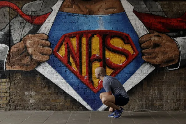A jogger stops to tie his shoelace next to a recently painted NHS (National Health Service) Superman design mural by street artist Lionel Stanhope during the coronavirus lockdown, in the Waterloo area of London, Sunday, May 3, 2020. The highly contagious COVID-19 coronavirus has impacted on nations around the globe, many imposing self isolation and exercising social distancing when people move from their homes. (Photo by Matt Dunham/AP Photo)