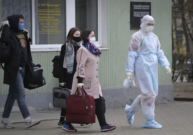 A medical worker wearing a protective suit accompanies students into an ambulance in Minsk, Belarus, Tuesday, April 21, 2020. The World Health Organization is urging the government of Belarus to cancel public events and implement measures to ensure physical and social distancing amid the growing coronavirus outbreak. (Photo by Sergei Grits/AP Photo)