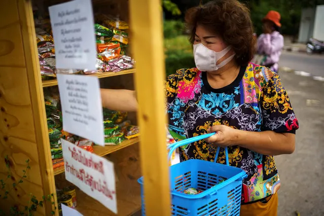 A woman in a protective mask puts foods inside a food pantry for people who are affected by the government's measures against the coronavirus disease (COVID-19) at a community in Bangkok, Thailand, May 11, 2020. (Photo by Athit Perawongmetha/Reuters)