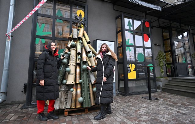 Two women pose for a photograph next to a symbolic Christmas tree made from spent shells casing and other spent ammunition erected outside a cafe in the center of Kyiv on December 18, 2023, amid Russian invasion in Ukraine. (Photo by Sergei Supinsky/AFP Photo)