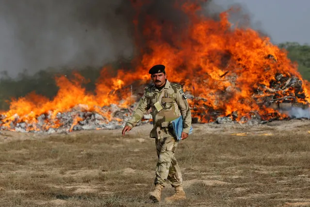 A soldier walks past a burning pile of confiscated heroin, hashish and opium during a drugs destruction ceremony to mark the International Day against Drug Abuse and Illicit Trafficking, which is held every year on June 26, but delayed due to the holy month of Ramadan, organized by the Pakistan Coast Guards (PCG) on the outskirts of Karachi, Pakistan November 13, 2017. (Photo by Akhtar Soomro/Reuters)