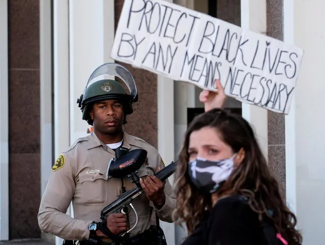 A demonstrator holding a sign stands against a Los Angeles County sheriff's deputy in a protest against the death of 18-year-old Andres Guardado and racial injustice, in Compton, California, June 21, 2020. (Photo by Ringo Chiu/Reuters)