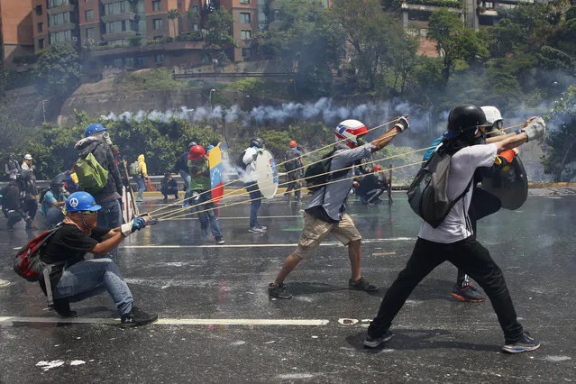 Anti-government protesters work together to aim a giant slingshot holding a glass bottle of fecal matter, at security forces blocking their march from reaching the Supreme Court in Caracas, Venezuela, on May 10, 2017. (Photo by Ariana Cubillos/AP Photo)