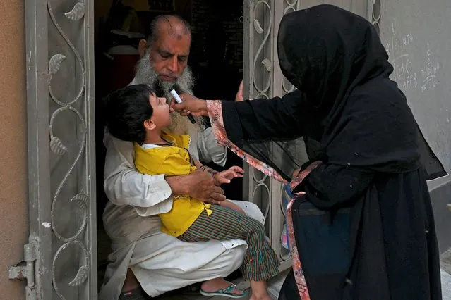 A health worker administers polio vaccine drops to a child during a polio vaccination door-to-door campaign in Lahore, Pakistan on August 16, 2020. (Photo by Arif Ali/AFP Photo)