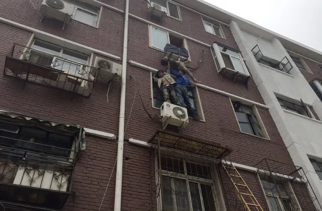 Liu Xinjun (L) and Jia Xiaoyu (R) hold a woman who fell out a window at her home in Tianjin, China, June 17, 2014. Liu and Jia held up an elderly who fell out her window and was stuck on a rack of an air-conditioner for five minutes, as another man Yang Ming held on to the woman with a rope from inside the room while waiting for firefighters to rescue. (Photo by Reuters/China Daily)