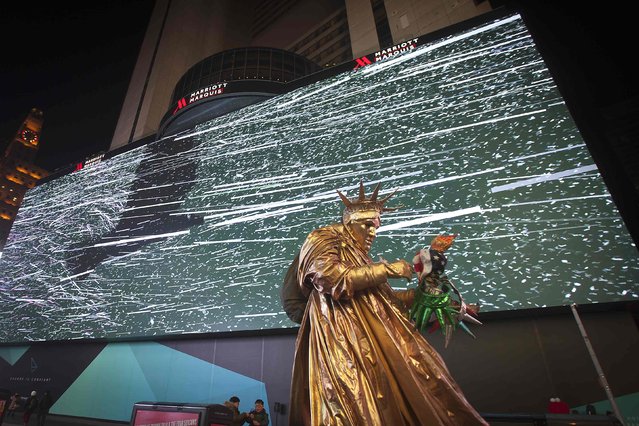 A man dressed up as the Statue of Liberty walks in front of a new digital advertising screen in Times Square, New York, November 18, 2014. (Photo by Carlo Allegri/Reuters)