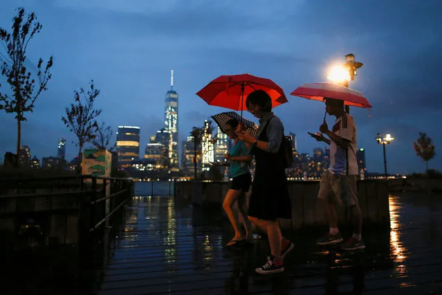 People walk through a park along the Hudson River across from New York's Lower Manhattan and One World Trade Center as rain falls in Exchange Place, New Jersey, U.S., July 30, 2016. (Photo by Eduardo Munoz/Reuters)