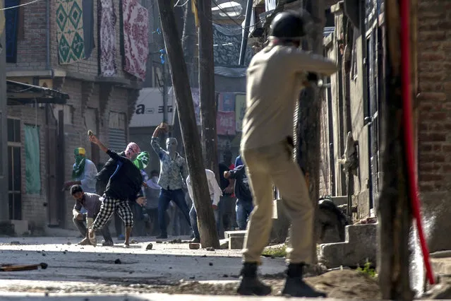 Kashmiri protesters throw stones and bricks at an Indian policeman as he prepares to fire pallet gun during a protest in Srinagar, Indian controlled Kashmir, Friday, October 7, 2016. Authorities imposed a curfew in many parts of the Indian-controlled Kashmir to prevent a protest march to the disputed Himalayan region's office of United Nations Military Observer Group in India and Pakistan (UNMOGIP) called by separatist leaders seeking end of Indian rule. (Photo by Dar Yasin/AP Photo)