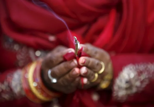 A devotee holds a burning incense while offering prayer to the setting sun during the "Chhat" festival at Bagmati river in Kathmandu, Nepal November 17, 2015. Hindus in Nepal celebrate "Chhat", a four-day festival that honours the sun god, by praying at sunrise and sunset, and seek blessings for one's family by giving offerings. (Photo by Navesh Chitrakar/Reuters)