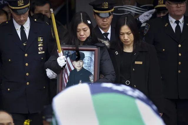 Widow Pei Xia Chen holds a photo of slain New York Police Department officer Wenjian Liu as his casket departs his funeral in the Brooklyn borough of New York January 4, 2015. New York Mayor Bill de Blasio appealed for reconciliation on Sunday in his eulogy for the second of two police officers murdered last month, two deaths that led to accusations the mayor had contributed to an anti-police climate. (Photo by Carlo Allegri/Reuters)