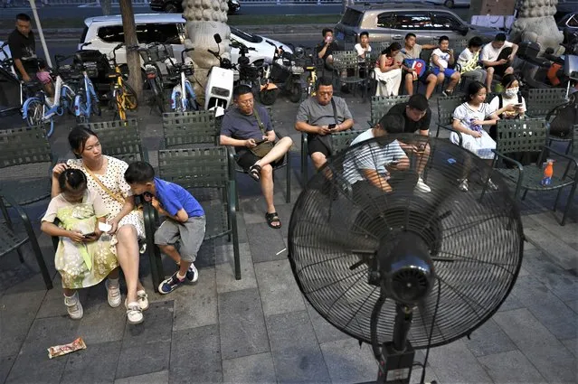 People sit in front of a fan as they wait for seats at a restaurant during heatwave conditions in Beijing on July 19, 2023. (Photo by Greg Baker/AFP Photo)