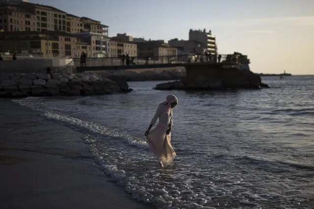 A woman dips her feet in the sea before curfew at Marseille's Plage des Catalans, southern France, Sunday, February 28, 2021. (Photo by Daniel Cole/AP Photo)