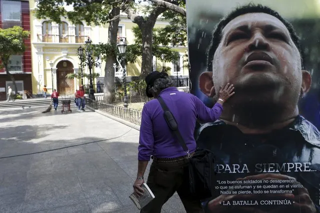 A man touches a portrait of Venezuela's late President Hugo Chavez as he walks next to it at the Plaza Bolivar near the building housing the National Assembly in Caracas January 8, 2016. (Photo by Marco Bello/Reuters)