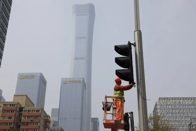 A worker installs new traffic lights at a junction in Beijing on Thursday, April 15, 2021. (Photo by Ng Han Guan/AP Photo)