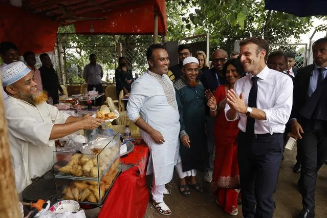 France's President Emmanuel Macron (4R) gestures towards a street vendor (2L) offering snacks during his two-day visit in Dhaka on September 11, 2023. (Photo by Ludovic Marin/AFP Photo)