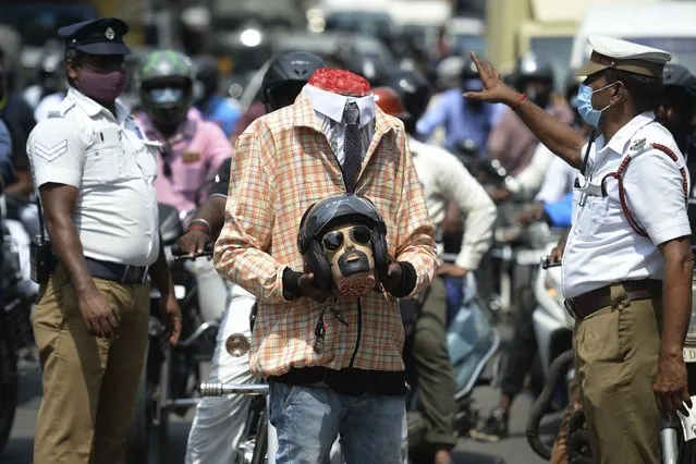 Police officers along with a volunteer (C) dressed up as a motorcyclist holding a mockup head with a helmet take part in a road safety awareness campaign, in Chennai on July 7, 2021. (Photo by Arun Sankar/AFP Photo)