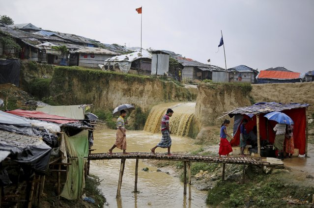 In this photograph taken August 28, 2018, sewer water flows in the back as Rohingya refugees cross a makeshift bamboo bridge at Kutupalong refugee camp, Bangladesh. (Photo by Altaf Qadri/AP Photo)