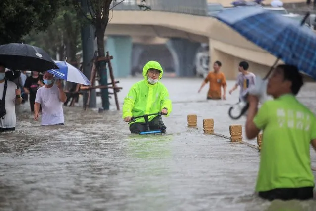 This photo taken on July 20, 2021 shows a man riding a bicycle through flood waters along a street following heavy rains in Zhengzhou in China's central Henan province. (Photo by AFP Photo/China Stringer Network)