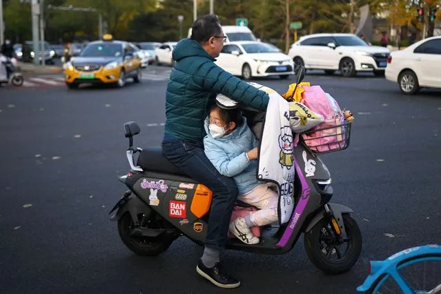 A child looks back from an electric scooter while returning from school in Beijing on November 22, 2023. (Photo by Wang Zhao/AFP Photo)