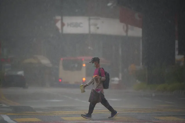 A food delivery worker wearing face mask delivering food during heavy downpour in downtown Kuala Lumpur, Malaysia, Thursday, July 8, 2021. Malaysia starts further tightening movement curbs and imposes a curfew in most areas in its richest state Selangor and parts of Kuala Lumpur, where coronavirus cases remain high despite a national lockdown last month. (Photo by Vincent Thian/AP Photo)