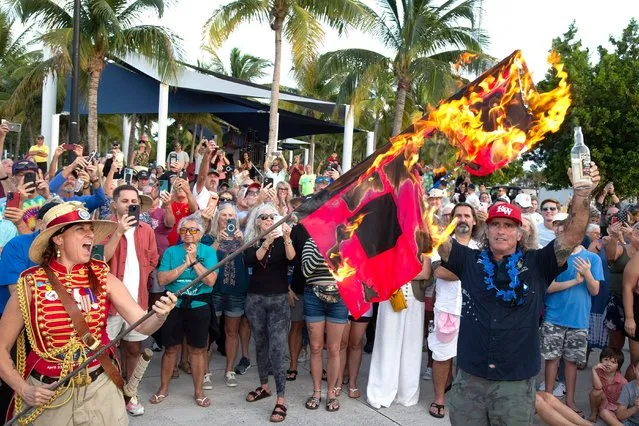 In this photo provided by the Florida Keys News Bureau, Jai Somers, left, holds hurricane warning flags aloft as they burn after being doused with rum by Paul Menta, right, to mark the end of the 2023 Atlantic hurricane season Thursday, November 30, 2023, in Key West, Fla. According to the National Hurricane Center, this year's above-normal Atlantic hurricane season was characterized by record warm Atlantic Ocean sea surface temperatures and a strong El Nino. The Atlantic basin saw 20 named storms in 2023. (Photo by Carol Tedesco/Florida Keys News Bureau via AP Photo)