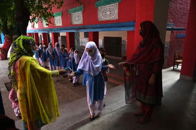 A teacher sprays sanitzer (R) while a colleague checks the body temperature of a student in a queue as they arrive at a school in Lahore on September 16, 2021, after the government reopened educational institutes that were closed as a preventive measure to curb the spread of the Covid-19 coronavirus. (Photo by Arif Ali/AFP Photo)