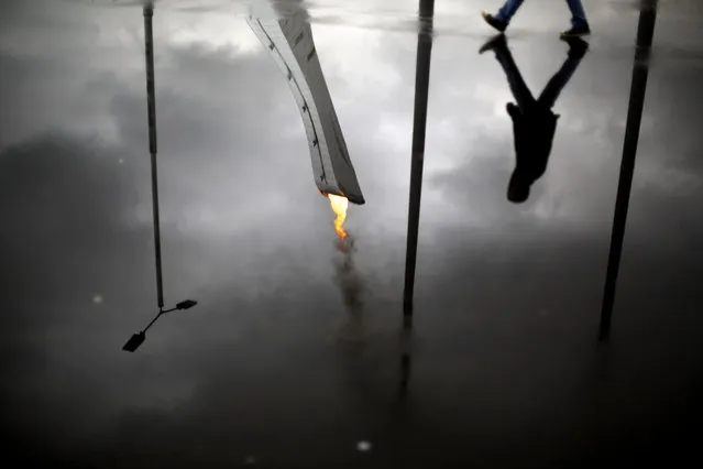 The Olympic flame is reflected in a puddle while lit during a test in the Olympic Park for the upcoming 2014 Winter Olympics as a pedestrian passes by, Friday, January 31, 2014, in Sochi, Russia. (Photo by David Goldman/AP Photo)